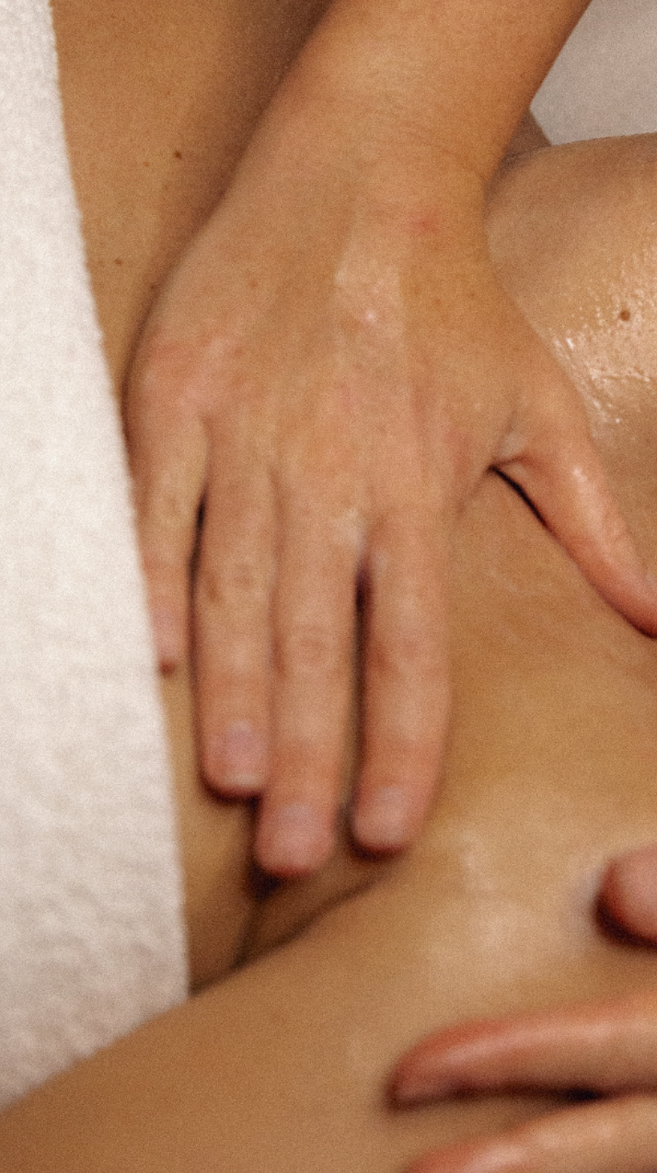 Nahaufnahme: Hände massieren mit Öl einen Oberschenkel, daneben ein weißes Frotteetuch – Lymphdrainage Beine selber machen